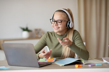 Positive blonde girl teenager having video conference with teacher