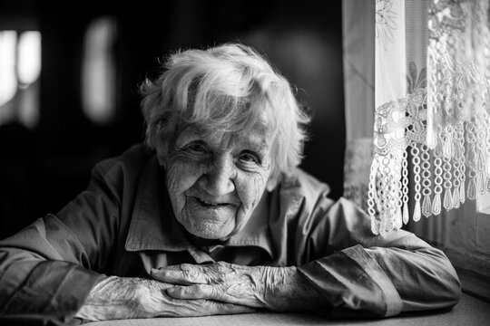 An old woman in the house sitting at the table. Black and white photo.