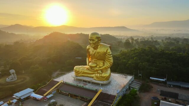 4k Stunning statue of Luang Phor Thuat at dawn, biggest in the world. Khao Yai mountains, Thailand. Sun glares at dawn. Buddhist park, wat. Golden image of Luang Phor Thuat