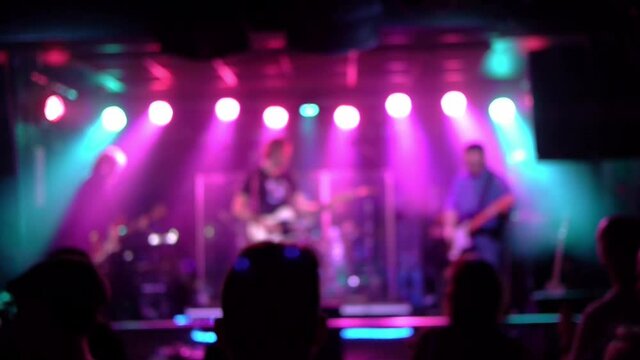 Band play rock at a club. Picture out of focus while the audience applauds. Smoke and light from the stage. Two guitars and a bass.