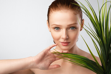 Naklejka premium Ginger-Haired Young Lady Posing Touching Green Plant On Gray Background
