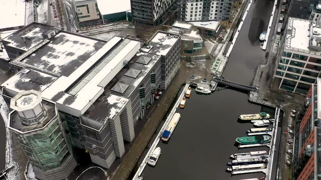 Aerial footage of a snowy winters day in the city of Leeds in the UK showing the area in Leeds known as the Leeds Dock near the Leeds and Liverpool canal and the Royal Armouries Museum covered in snow