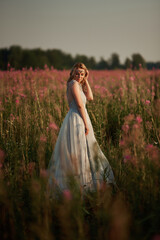 Romantic blonde woman running in a wonderful flower field. Warm sunset colors. Blue dress. Soft colors.