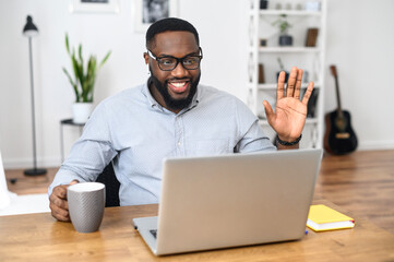 Happy and excited African-American business coach in glasses sitting at the desk, working from...