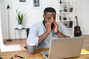 Desperate young African-American business entrepreneur in smart casual attire, touching the face,...