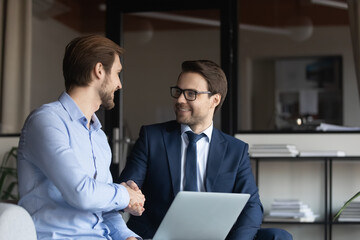 Close up smiling businessmen shaking hands, business partners making deal, agreement, sitting in...