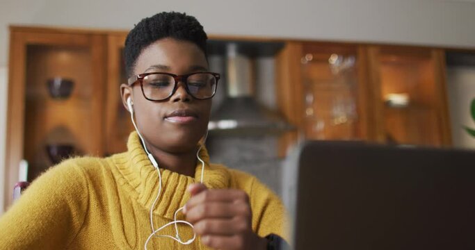 African american woman wearing earphones using laptop while working from home