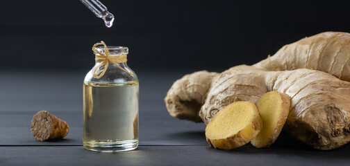 Glass bottle of essential ginger oil, ginger root and powder on black wooden rustic background, oil...