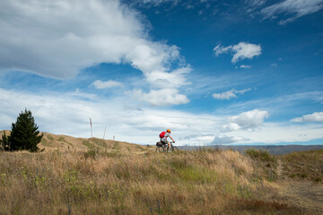 A young man cycling the Otago Central Rail Trail under the white clouds, at Chatto Creek.
