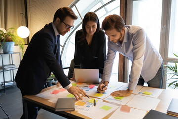 Diverse colleagues working with financial documents, writing notes on colorful stickers, project statistics in office, Indian businesswoman with coworkers developing business strategy, teamwork