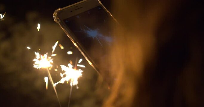 Girl lightening Christmas sparklers and taking photos with smartphone. Close up