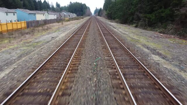 Moving fast down train tracks through residential neighborhood close to homes
