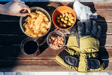 A woman's hand grabs a potato chip from a snack table on a rustic board in the snow. Winter concept. Food concept.