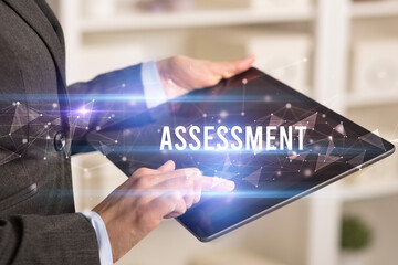 Close up hands using tablet with ASSESSMENT inscription, modern business technology concept