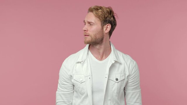 Secret bearded young man 20s in white casual clothes isolated on pastel pink background studio. People lifestyle concept. Looking aside saying hush be quiet with finger on lips shhh gesture blinking