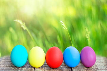 colorful easter eggs on wooden table on green grass background with bokeh. copy space
