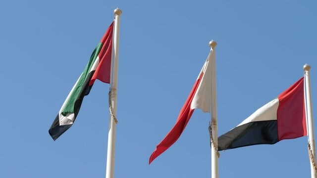 Flags of Dubai and UAE fluttering in wind against blue sky. Static, low angle