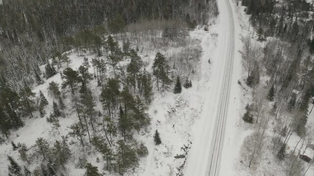 A quiet serene winterscape of a train rail system cutting through the frozen Canadian boreal forest.  Snowing.  Aerial shot. 4k.