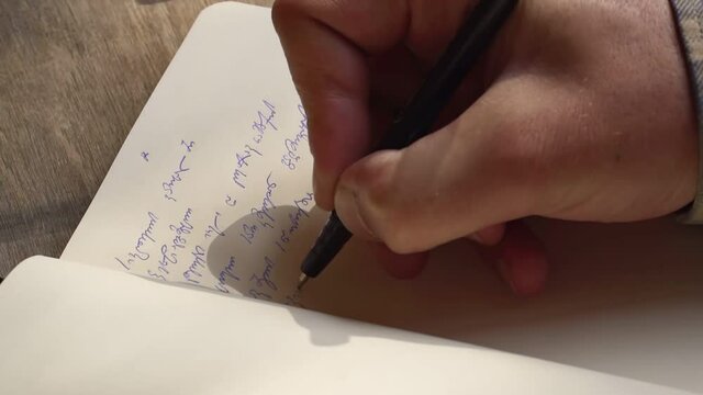 Person writing with a pen Georgian script on a notebook - High angle Close up