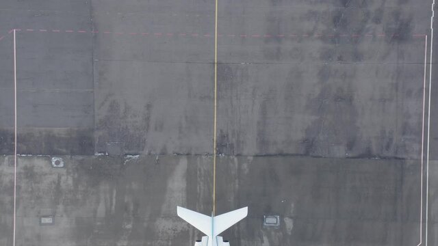 Top down aerial revealing white private jet parked on grey tarmac at airbase