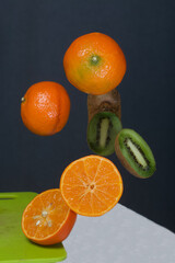 Tangerines and kiwis float above the table surface. Some are cut into pieces. Fruit levitation.