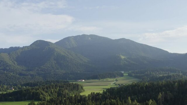 Aerial side track shot of mountain, forest, and fields in Kotlje