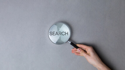 Woman holding magnifying glass on grey background, closeup. Find keywords concept