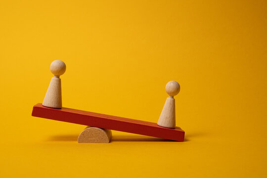 Seesaw with wooden figures. Yellow background
