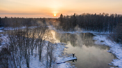 Fototapeta na wymiar Aerial drone image of the man standing on the bridge and admiring the sunset scenery of the heavily steaming natural spring on the freezing cold winter day