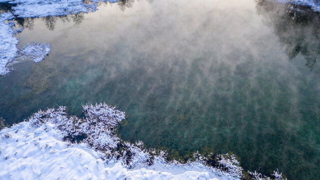 Aerial drone image of the natural groundwater spring scenery with the heavily steaming water during the freezing cold winter sunset