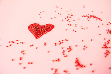 Composition of the heart as a symbol of love laid out from red beads on pink background for valentine's day.