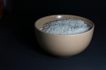 White uncooked rice in a bowl with scattered grains nearby on a black background
