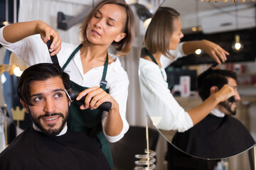 Fototapeta na wymiar female professional shaving cheerful male's hair in hairdressing salon