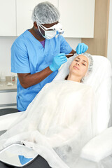Cosmetologist man in mask preparing woman client for mesotherapy procedure in medical office