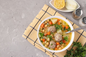 Turkish soup with chickpeas, meatballs and vegetables in a white bowl on a gray background. With place for text.