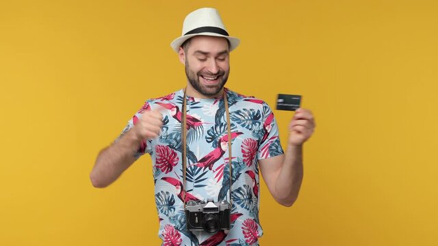 Excited traveler tourist man in summer clothes hat isolated on yellow background. Passenger traveling on weekend. Air flight journey concept. Pointing index finger on credit bank card showing thumb up