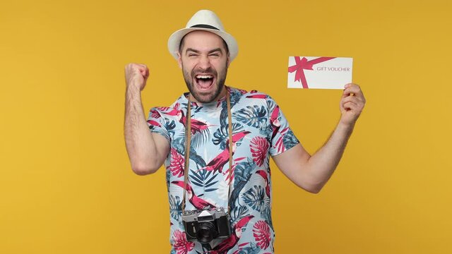 Surprised traveler tourist man in summer clothes hat isolated on yellow background. Passenger traveling on weekend. Air flight journey concept. Pointing finger on gift certificate doing winner gesture
