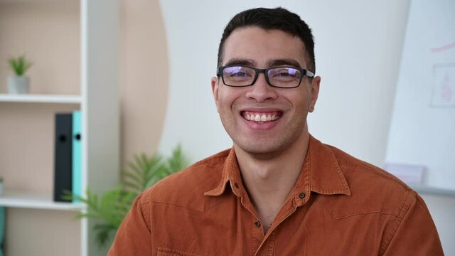 Attractive smart hispanic  guy, freelancer or teacher wearing eyeglasses, looks at the web camera with friendly smiling. Negotiation, online meeting concept