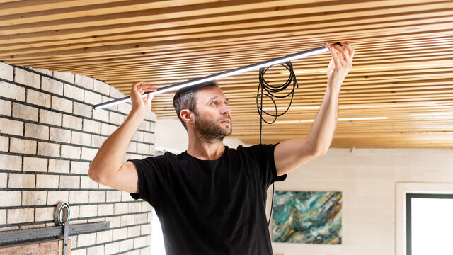 Electrician at work. Service for the repair of electrical wiring and replacement of ceiling lamps. A builder is installing a loft-style wooden ceiling. Rent-a-gent helps with the housework.