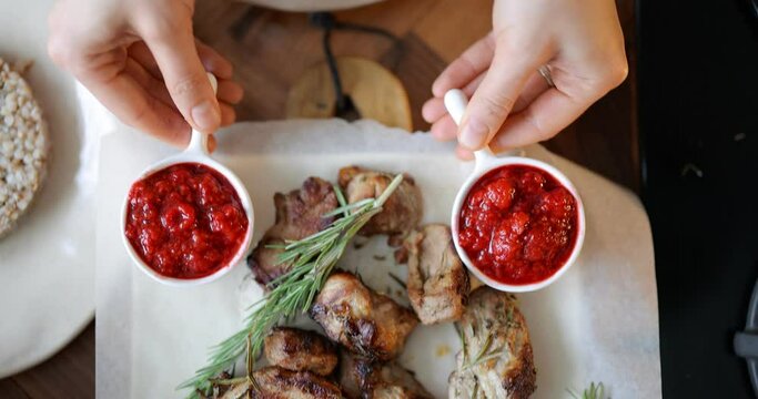 Woman putting raspberry gravy near the tasty cooked meat pieces on a plate. High angle tracking videoshot