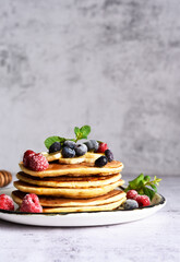 Homemade pancakes with banana, raspberries, blueberries and honey on a light kitchen background.
