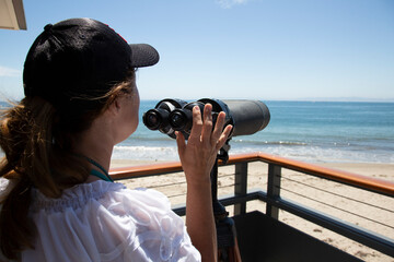Woman on deck with hand on powerful binoculars looking to the horizon of the ocean