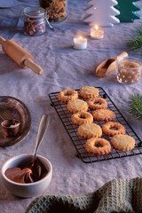 Sandwich cookies filled with hazelnut spread, nougat cream. Xmas trees, candles on linen tablecloth. Natural light.