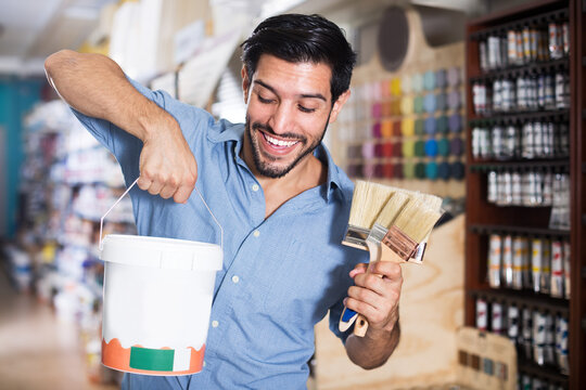 Happy male buyer holding bucket of paint and brushes in paint store