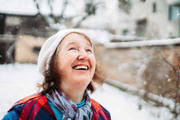 Elderly woman with white hat smiling and looking up while snow is falling