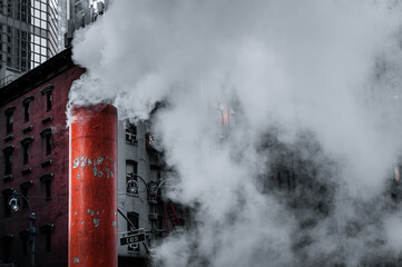 Close up view of the white-orange striped vent releasing steam on the street/ Old and modern buildings in the background.
Manhattan, New York, USA