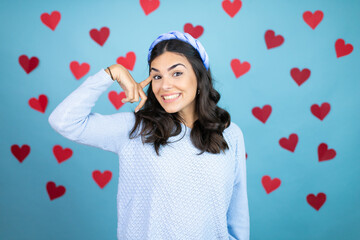 Young beautiful woman over blue background with red hearts smiling and thinking with her fingers on her head that she has an idea.