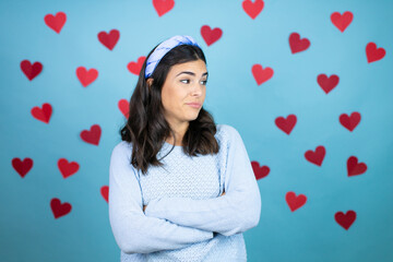 Young beautiful woman over blue background with red hearts thinking looking tired and bored with crossed arms