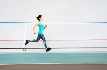 Sporty young woman running by all-season track at the stadium.