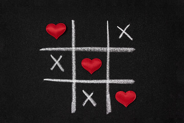 Red hearts and tic-tac-toe on black grainy cardboard. Love game concept.